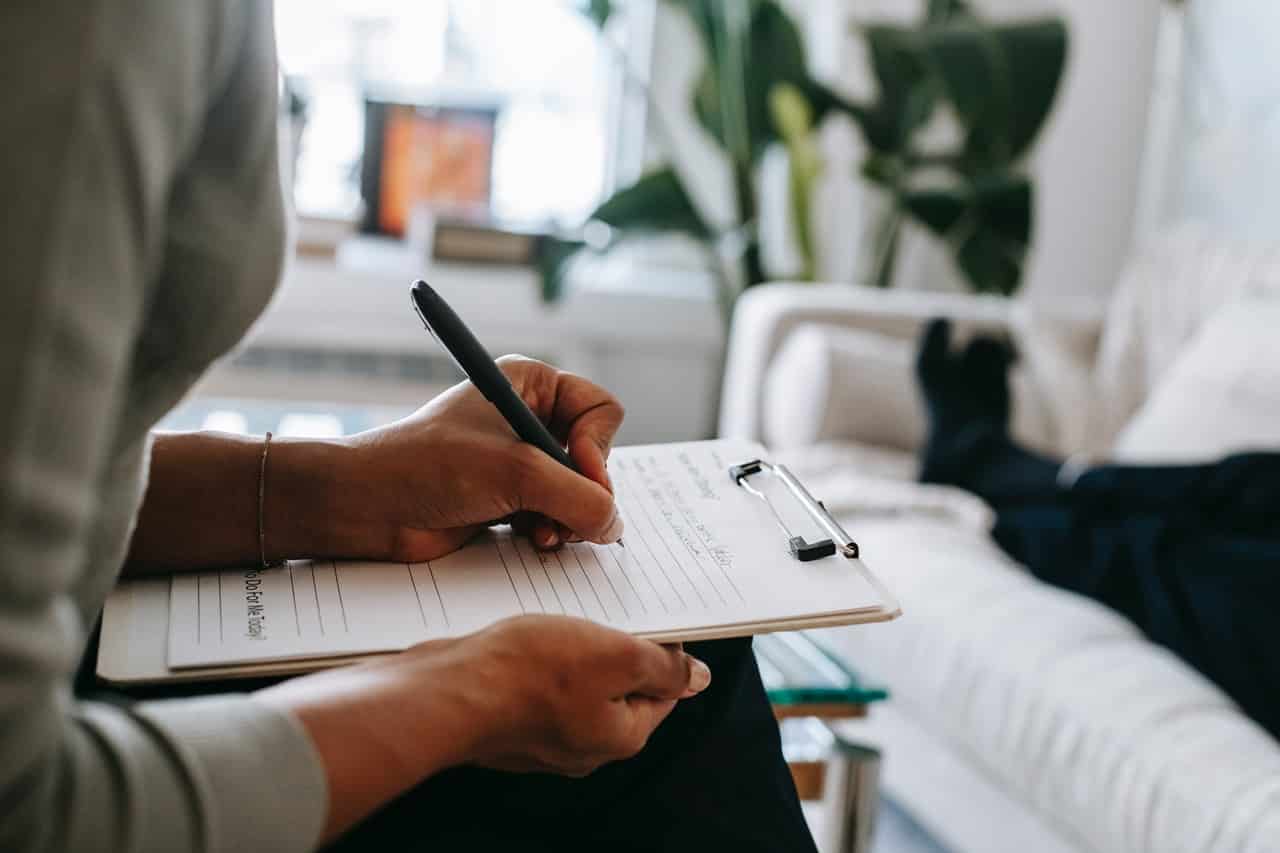 therapist writing on a clipboard while patient lies down on sofa
